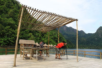 People sitting on railing by mountain against sky