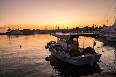 Boats moored in harbor at sunset