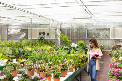 Woman standing by potted plants in greenhouse