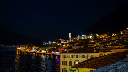 Illuminated buildings by river against sky at night