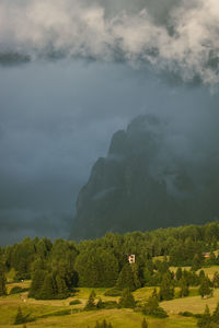 Meadow with cabin and trees during sunset against dark storm clouds