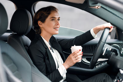 Businesswoman holding disposable coffee cup while driving car