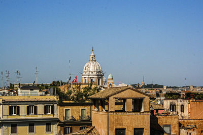 Tile-colored buildings and in the background is the dome of the vatican cathedral on a blue sky. 