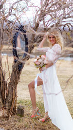 Portrait of smiling young woman standing by bare tree