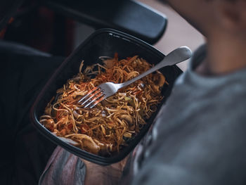 Young caucasian guy gamer holds with one hand a black wok food container with a fork