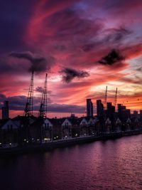 Buildings by river against sky at sunset