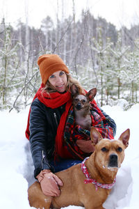 Beautiful smiling woman is on a walk with her two dogs in winter coniferous forest.