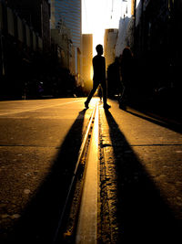 Silhouette people walking on railroad track at street in city during sunset