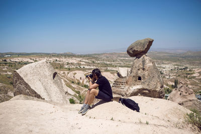 Photography man in a black t-shirt sitting on a rock and taking pictures of the views