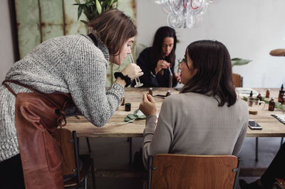 Mid adult owner smelling perfume in test tube by colleague at workshop