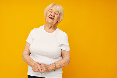 Portrait of young woman standing against yellow background