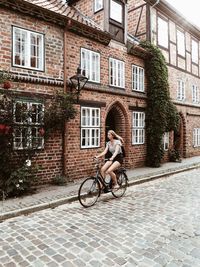 Full length of woman riding bicycle on street against building