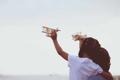 Mother and daughter flying toy airplane against clear sky