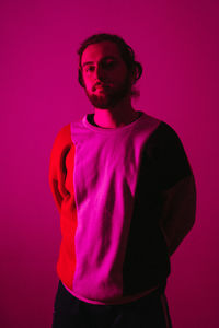 Portrait of young man standing against pink background