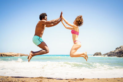 Full length of shirtless man jumping on beach