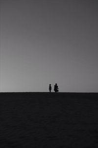 Silhouette father with son at beach against clear sky during sunset