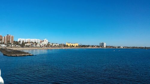 Sea by cityscape against clear blue sky