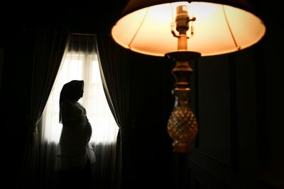 Woman standing in illuminated lamp at home