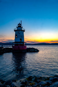 Lighthouse in sea against sky during sunset