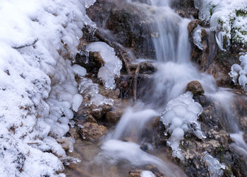 Frozen fast flowing spring water, icy rocks and water stream, frosty tree roots, beautiful ice 