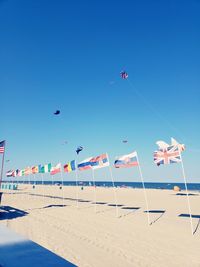 Various flags at beach against clear blue sky