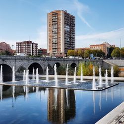 Arch bridge over river by buildings in city against sky