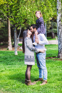 Father carrying daughter on shoulders while kissing mother in park