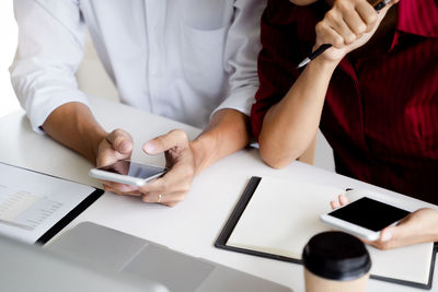 Midsection of man using mobile phone while sitting on table