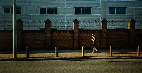 Full length of woman walking against brick wall