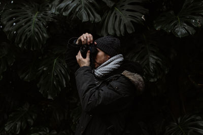 Midsection of man photographing against trees and plants