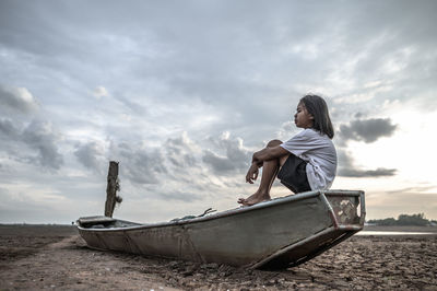 Side view of girl sitting in boat against sky