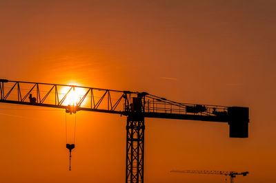 Silhouette cranes against sky during sunset