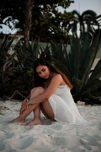 Full length of teenage girl sitting on sand at beach