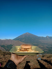 Midsection of person preparing food on mountain against clear blue sky