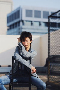 Portrait of young woman sitting on chair at building terrace