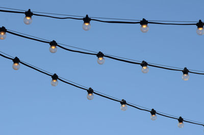 Strings of illuminated electric light bulbs outdoors against blue sky