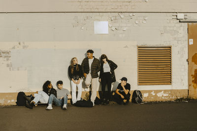 Young friends spending leisure time on footpath against wall