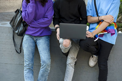 Young people with lgbt rainbow flag using laptop outdoors.