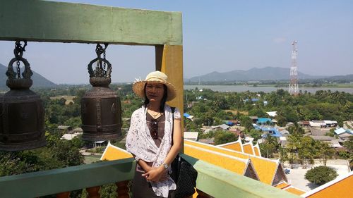 Portrait of smiling mature woman standing by bells at stupa against sky