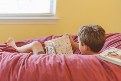 Boy with book relaxing on bed at home