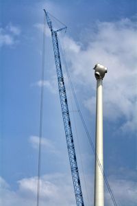 Incomplete windmill by crane against blue sky
