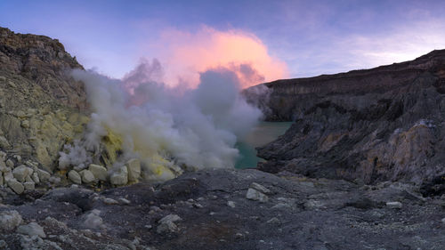 Hot spring by rocky cliff against sky during sunset