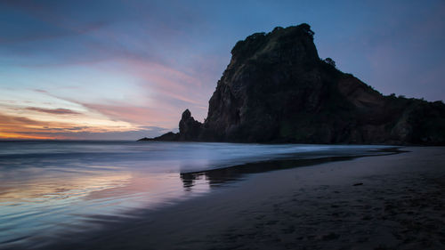 Rock formation on beach against sky during sunset