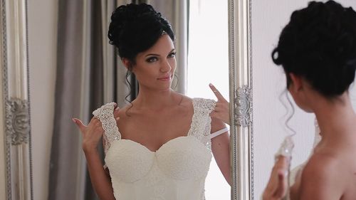 Reflection of bride trying wedding dress in fitting room on mirror