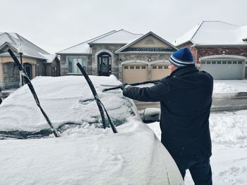 Rear view of man standing by car outdoors during winter