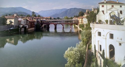 Arch bridge over river by buildings against sky