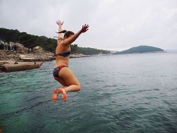 Full length of young woman wearing bikini diving in sea against sky