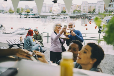 Smiling senior man and woman taking selfie amidst customers by food truck