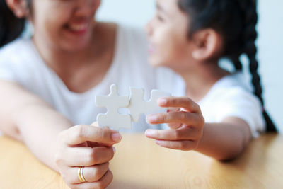 Midsection of mother with daughter solving jigsaw puzzle at table