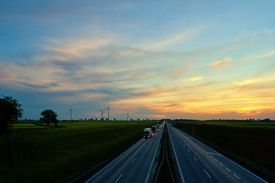 Highway with car traffic and windmill turbines at sunset
